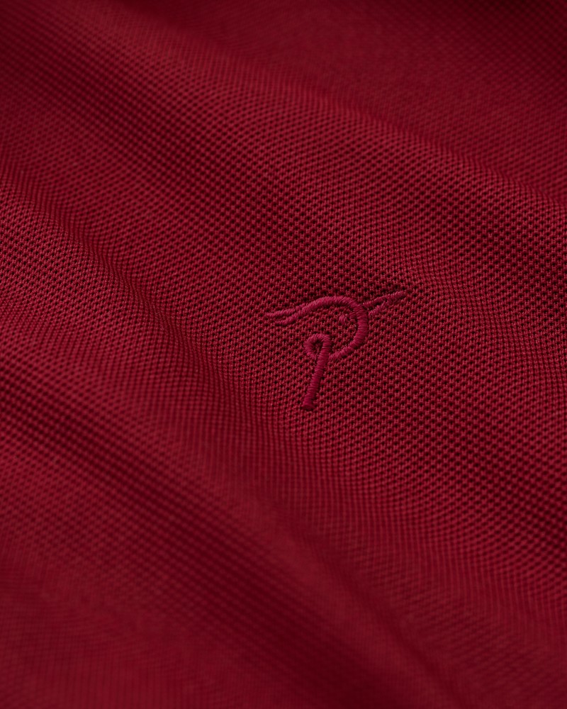 Zbliżenie haftowanego logo Pic à bec na bordowej tkaninie koszulki polo