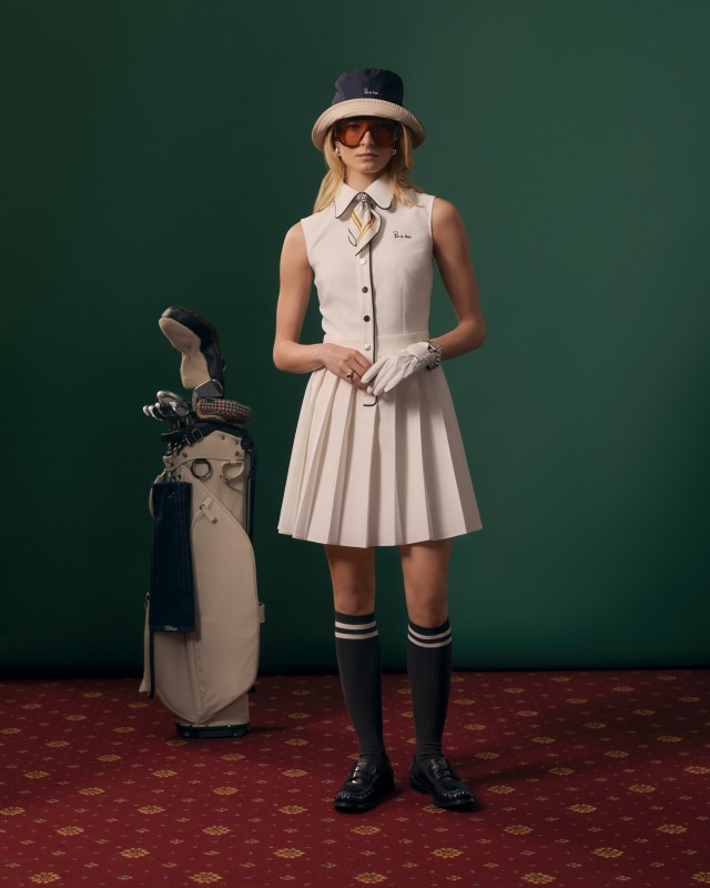 Modelka w ecru sukience golfowej bez rękawów z granatowym kapeluszem i getrami