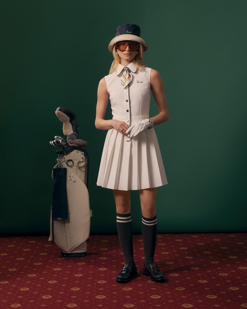 Modelka w ecru sukience golfowej bez rękawów z granatowym kapeluszem i getrami