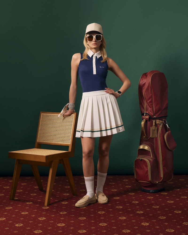 Modelka w granatowym polo bez rękawów i ecru plisowanej spódniczce, obok krzesła i torby golfowej