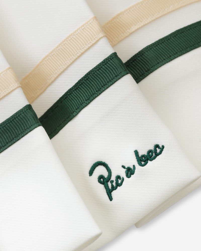 Zbliżenie haftowanego logo Pic à bec i pasków przy dole ecru spódniczki golfowej