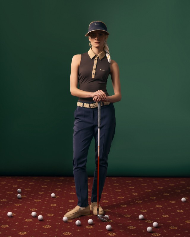 Modelka w brązowo-beżowym polo bez rękawów i granatowych wełnianych spodniach, z kijem golfowym