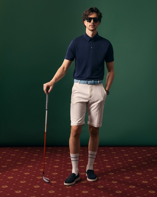 Mężczyzna w granatowym polo i białych szortach golfowych, z kijem golfowym