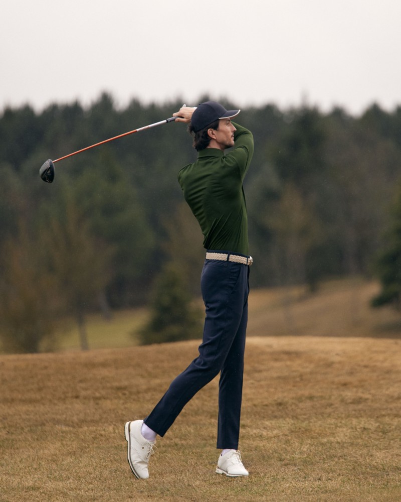 Mężczyzna w zielonym polo i granatowych spodniach golfowych podczas zamachu kijem golfowym