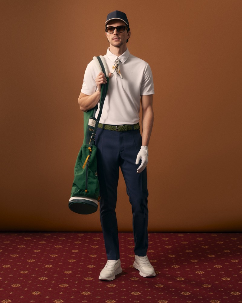 Mężczyzna w białym polo, granatowej czapce i granatowych spodniach golfowych, z zieloną torbą golfową