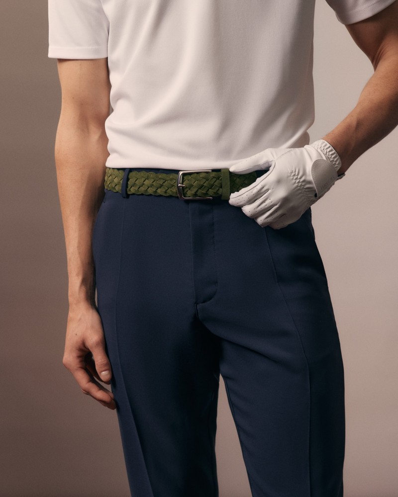 Zbliżenie zielonego plecionego paska na granatowych spodniach golfowych, dłoń w białej rękawiczce