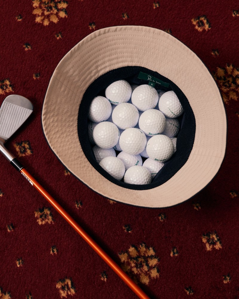 Kapelusz pełny piłek golfowych, obok kij do golfa